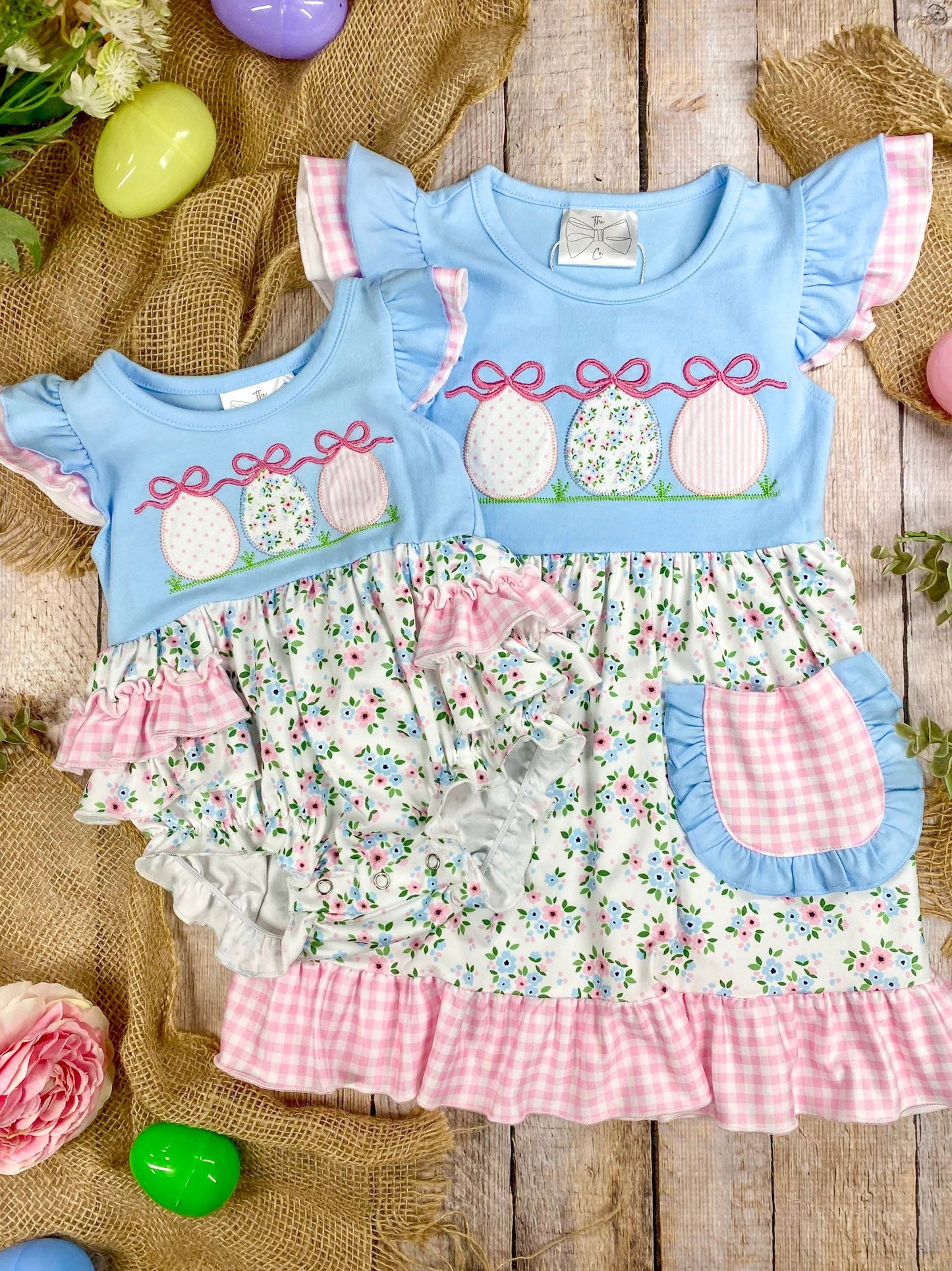 sibling set romper and dress with floral pattern and Easter eggs on a wooden surface with Easter decorations.