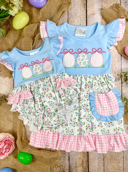 sibling set romper and dress with floral pattern and Easter eggs on a wooden surface with Easter decorations.