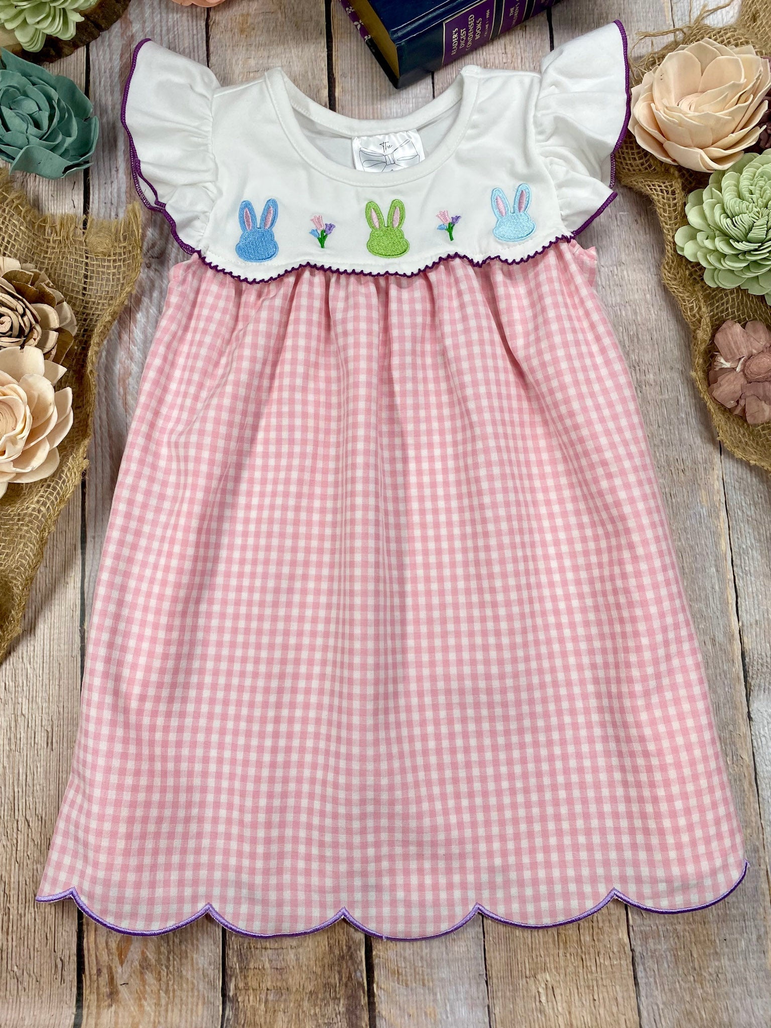 Pink gingham dress with embroidered bunny details on a wooden surface