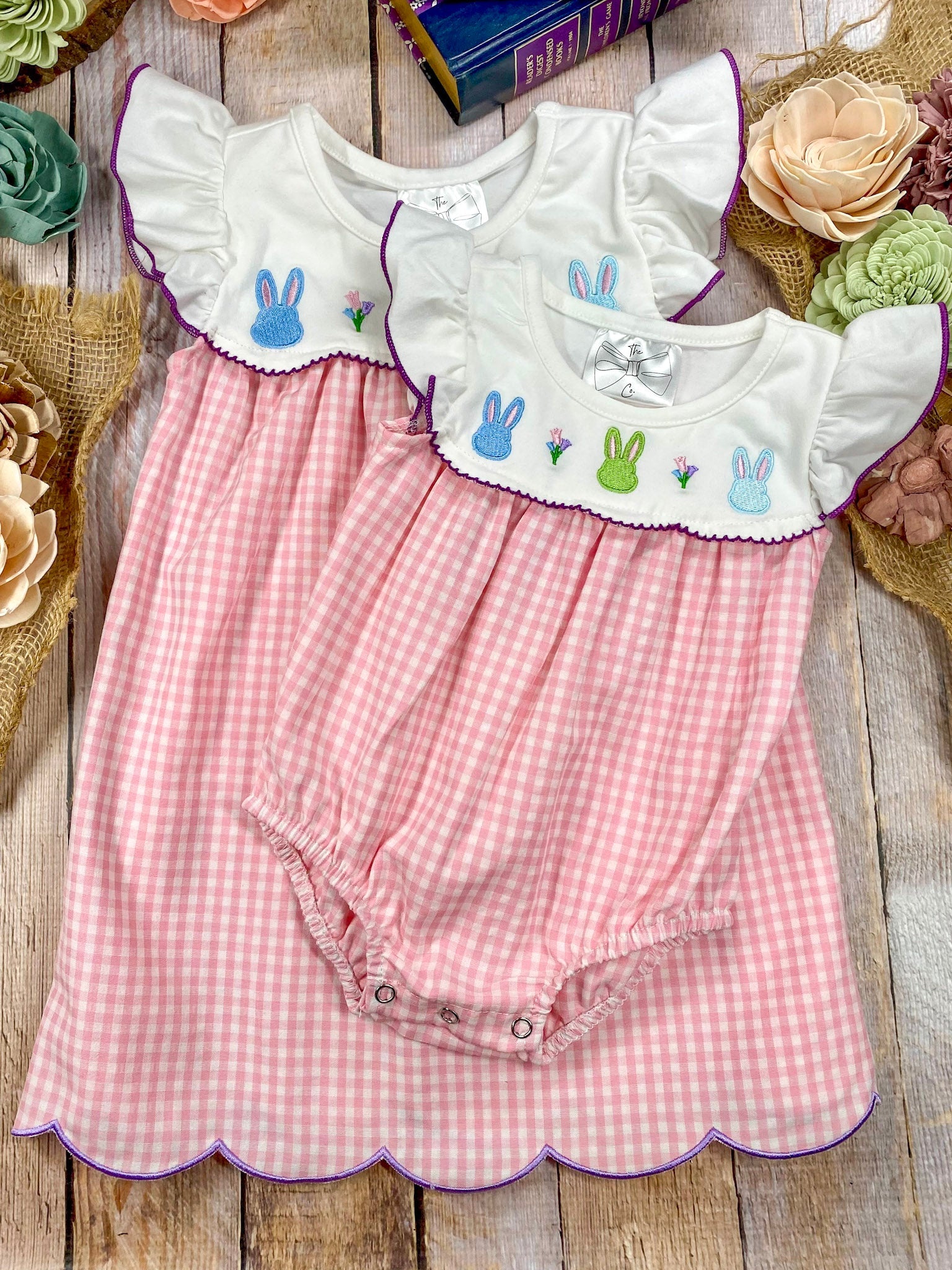 Pink checkered sibling dress and romper with embroidered bunny designs on a wooden surface