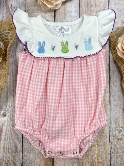 Pink gingham baby romper with embroidered bunnies on a wooden surface