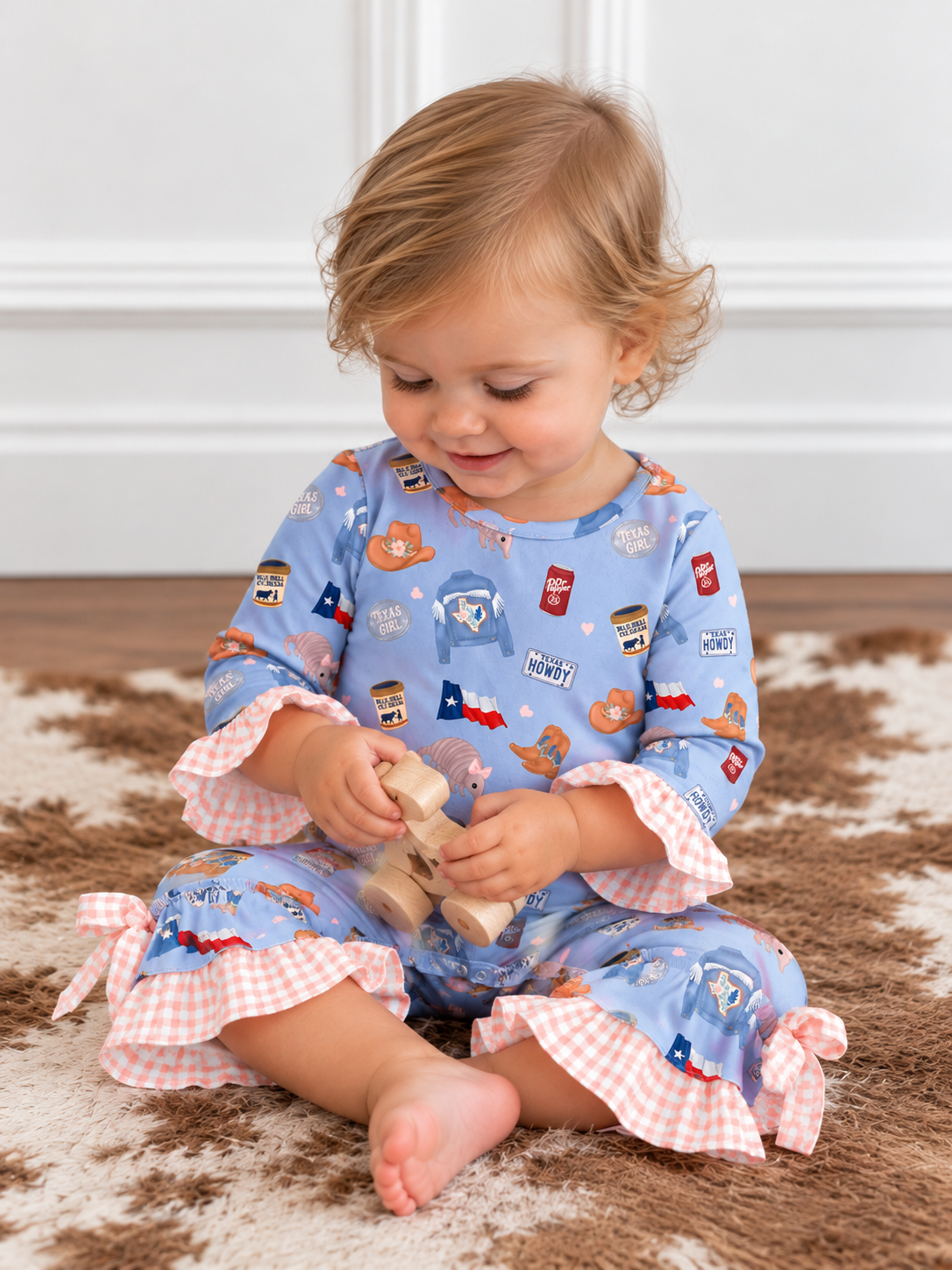 model wearing a Blue Texas print baby romper with pink gingham ruffles and bows at the ankles