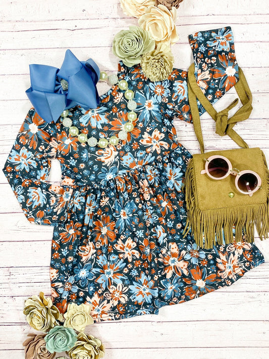 A flat lay of a floral twirl dress with long sleeves, accompanied by a blue bow and a yellow handbag with sunglasses.