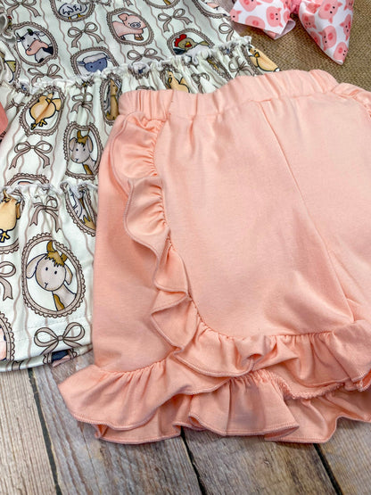 Children's outfit with patterned top and peach-colored shorts on a wooden background