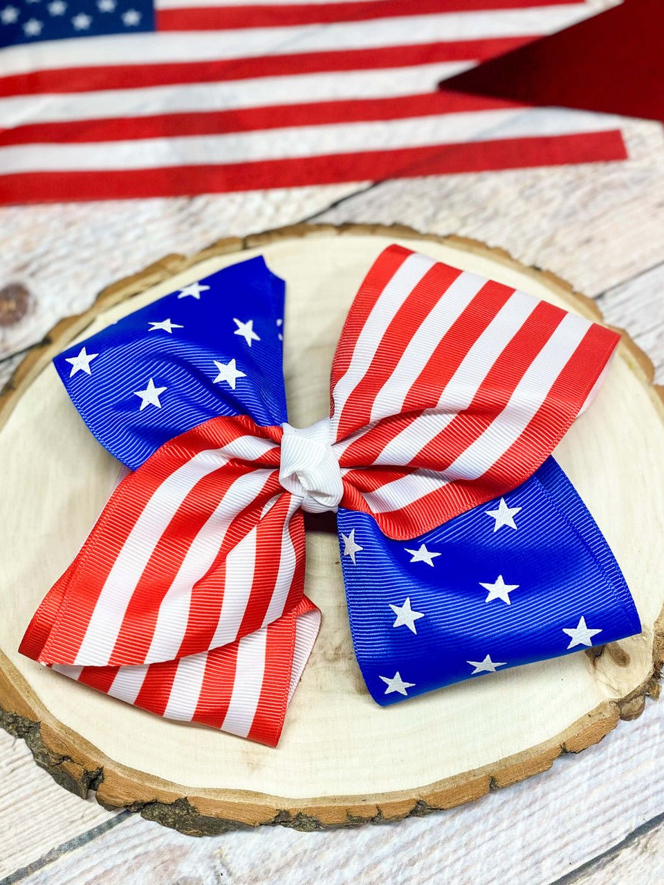 American flag-themed bow on a wooden surface with an American flag in the background.