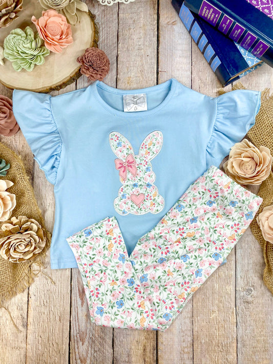 Light blue top with floral bunny design and matching pants on a wooden surface with decorative flowers.