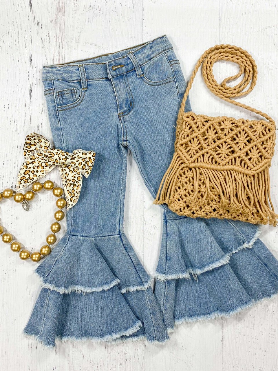 Frayed double bell bottom jeans laid flat with a gold bow and woven bag