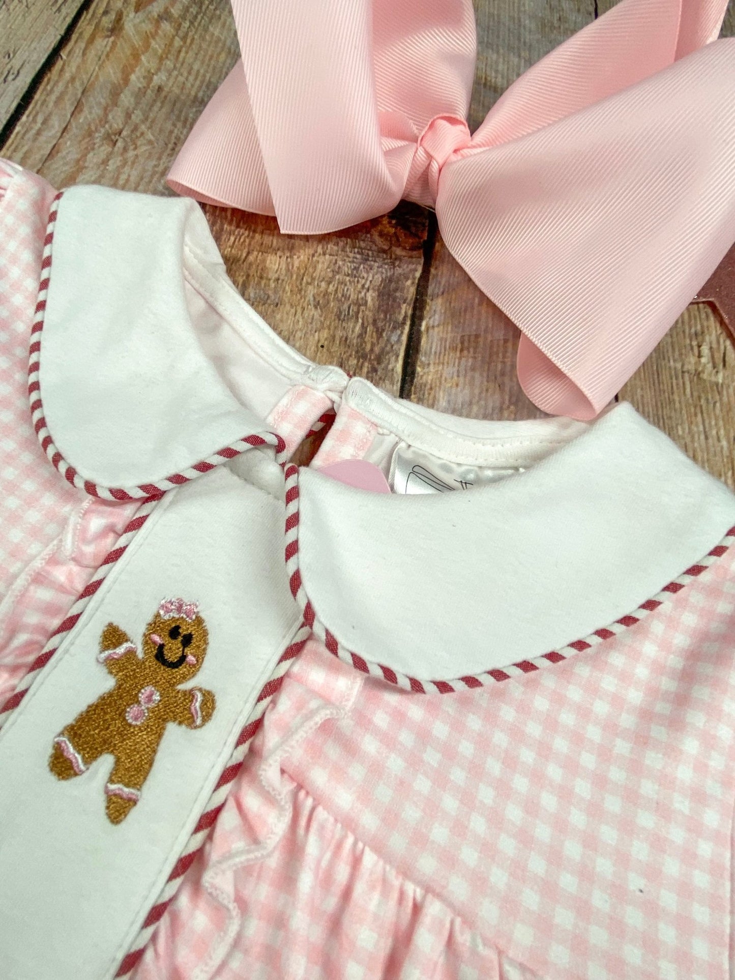 Close-up of a dress with a gingerbread man design and pink bow on a wooden surface