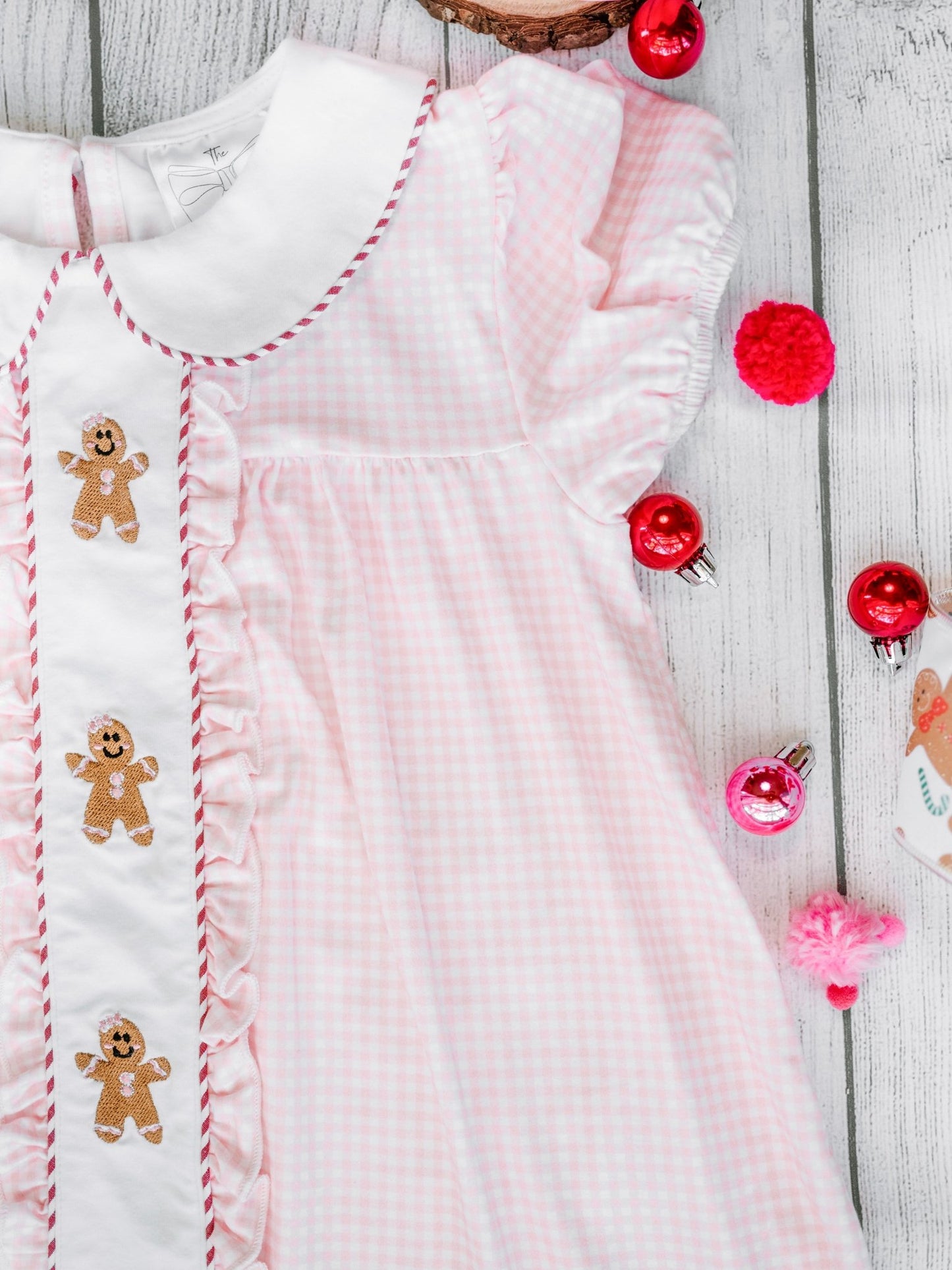 Pink baby dress with gingerbread man embroidery on a wooden surface with Christmas decorations.