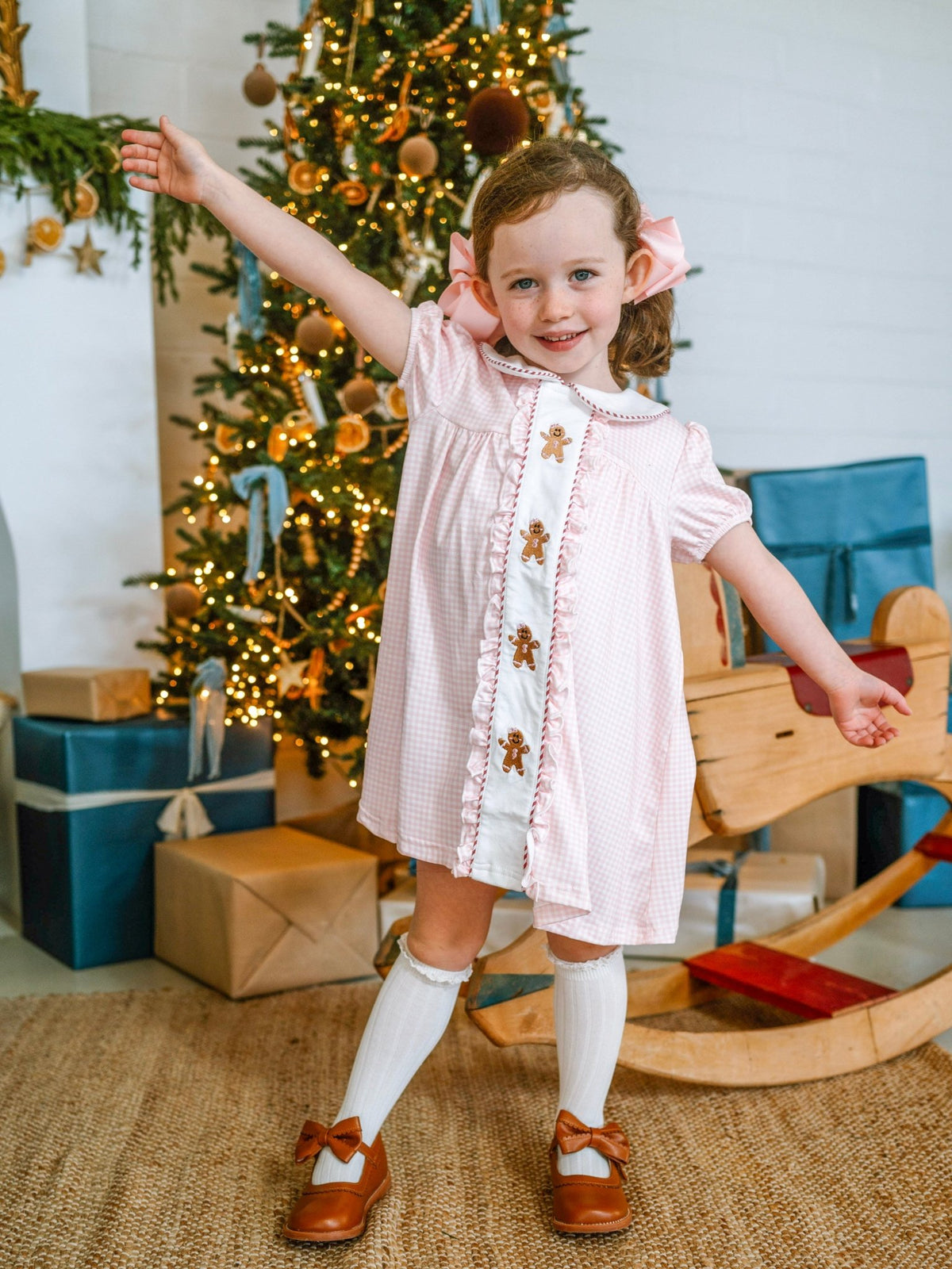 Girl wearing a pink gingham gingerbread dress by the Christmas tree