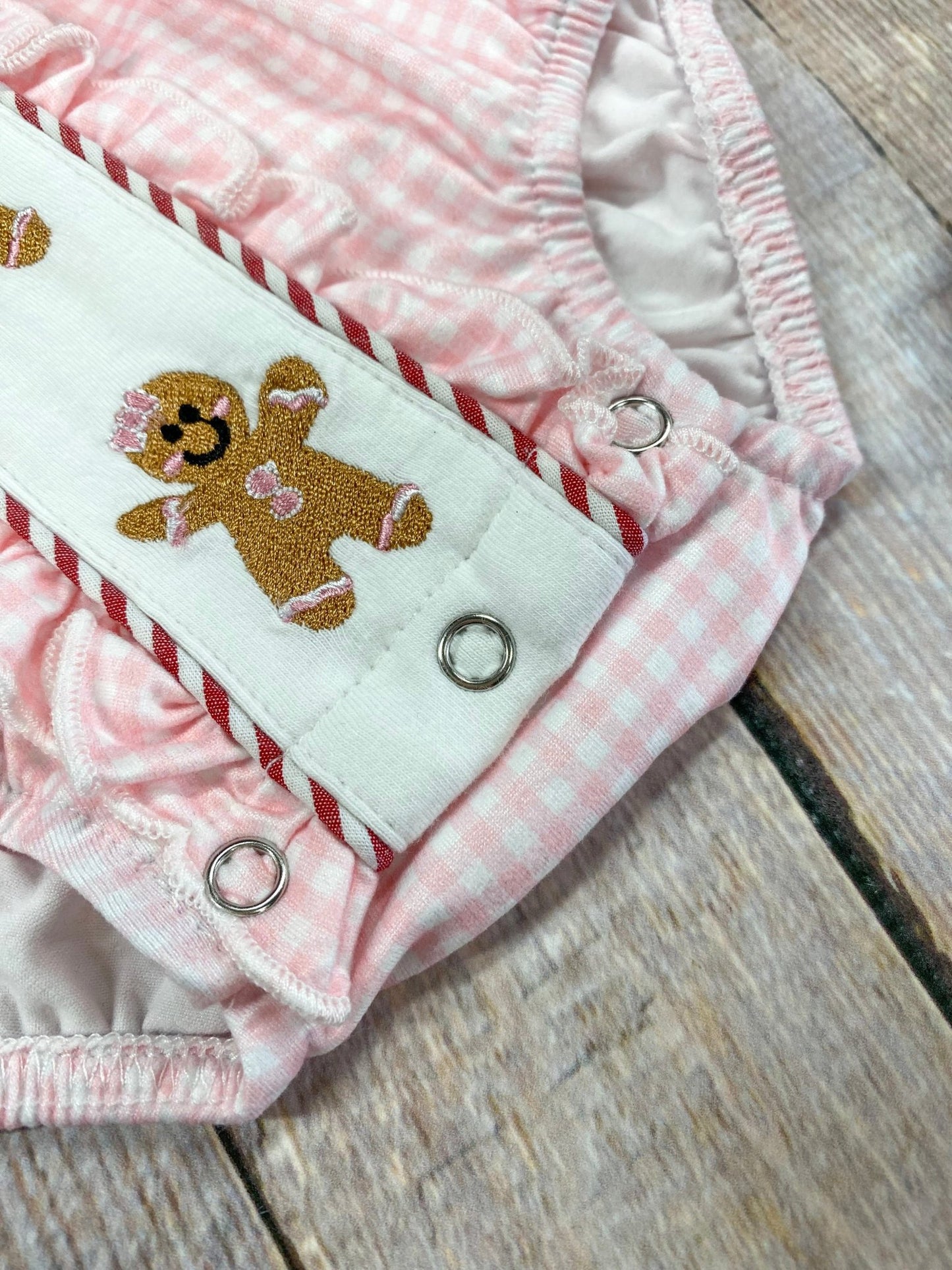 Pink baby romper with gingerbread design on a wooden surface