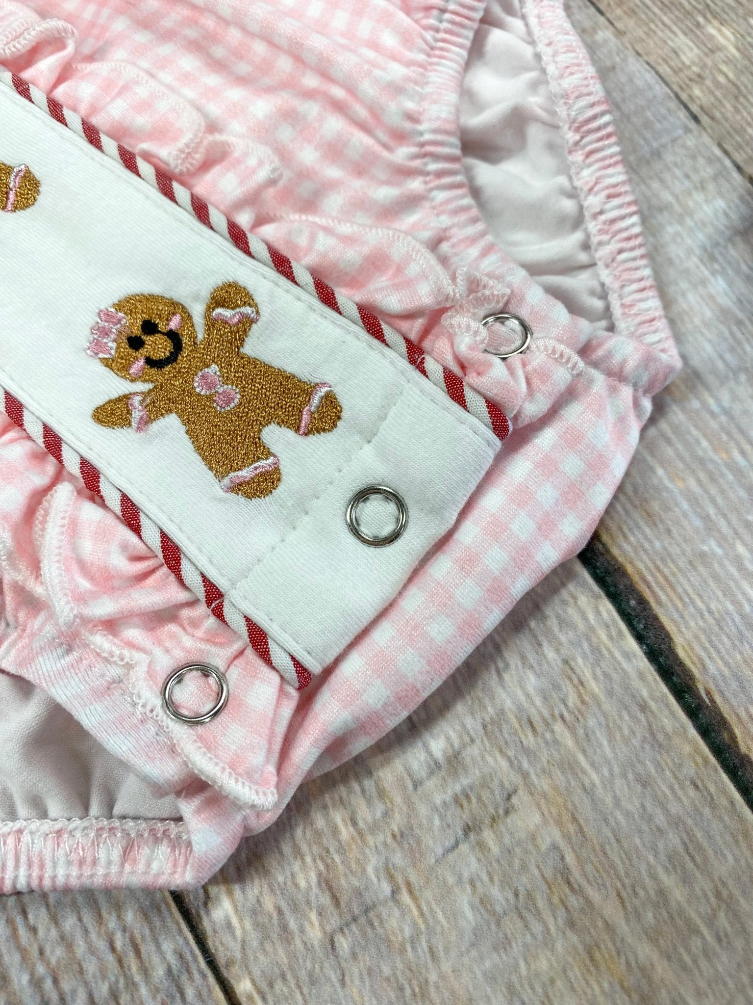 Pink baby romper with gingerbread design on a wooden surface