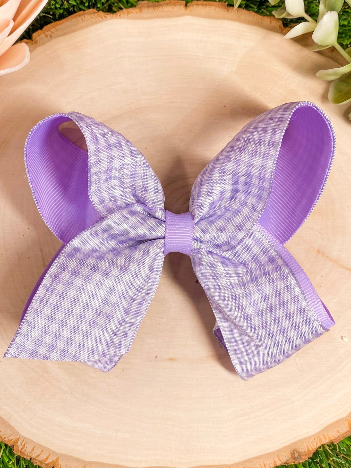 Purple and white checkered bow on a straw hat with grass in the background