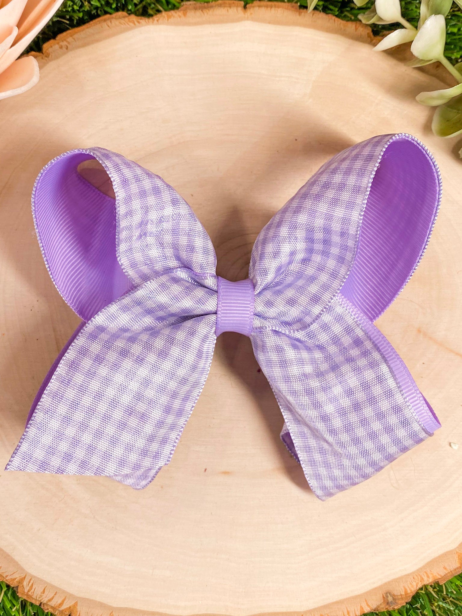 Purple and white checkered bow on a straw hat with grass in the background