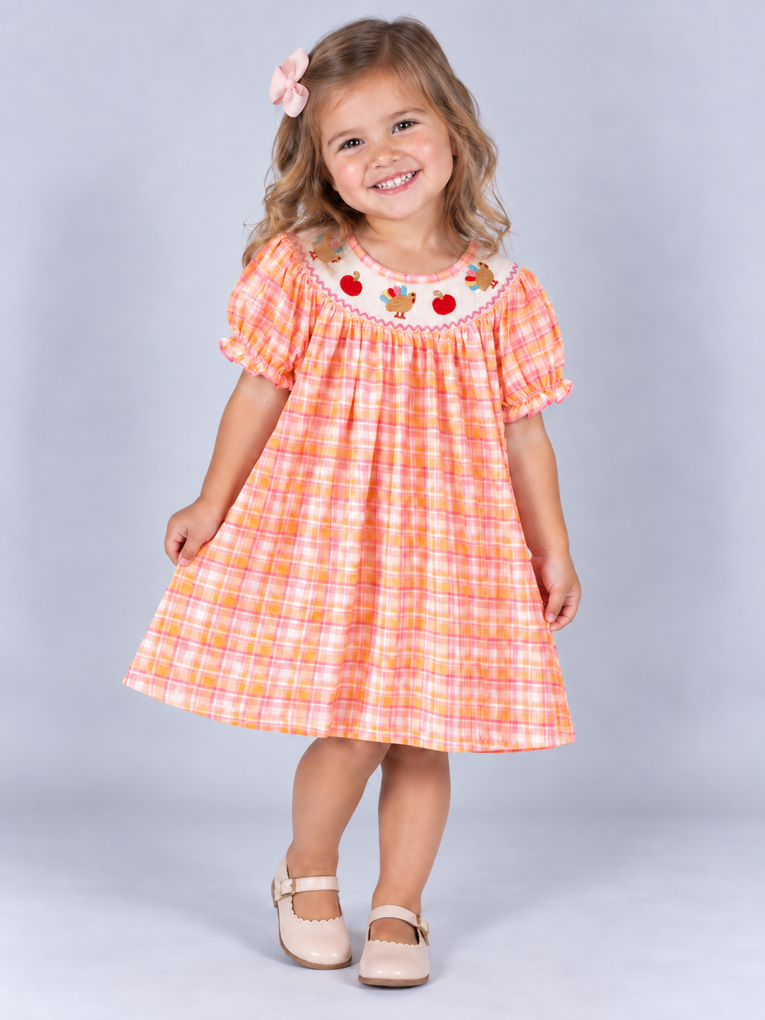 model wearing Pink and orange plaid girls’ Thanksgiving dress with a smocked neckline, embroidered turkeys and pumpkins, and ruffled sleeves