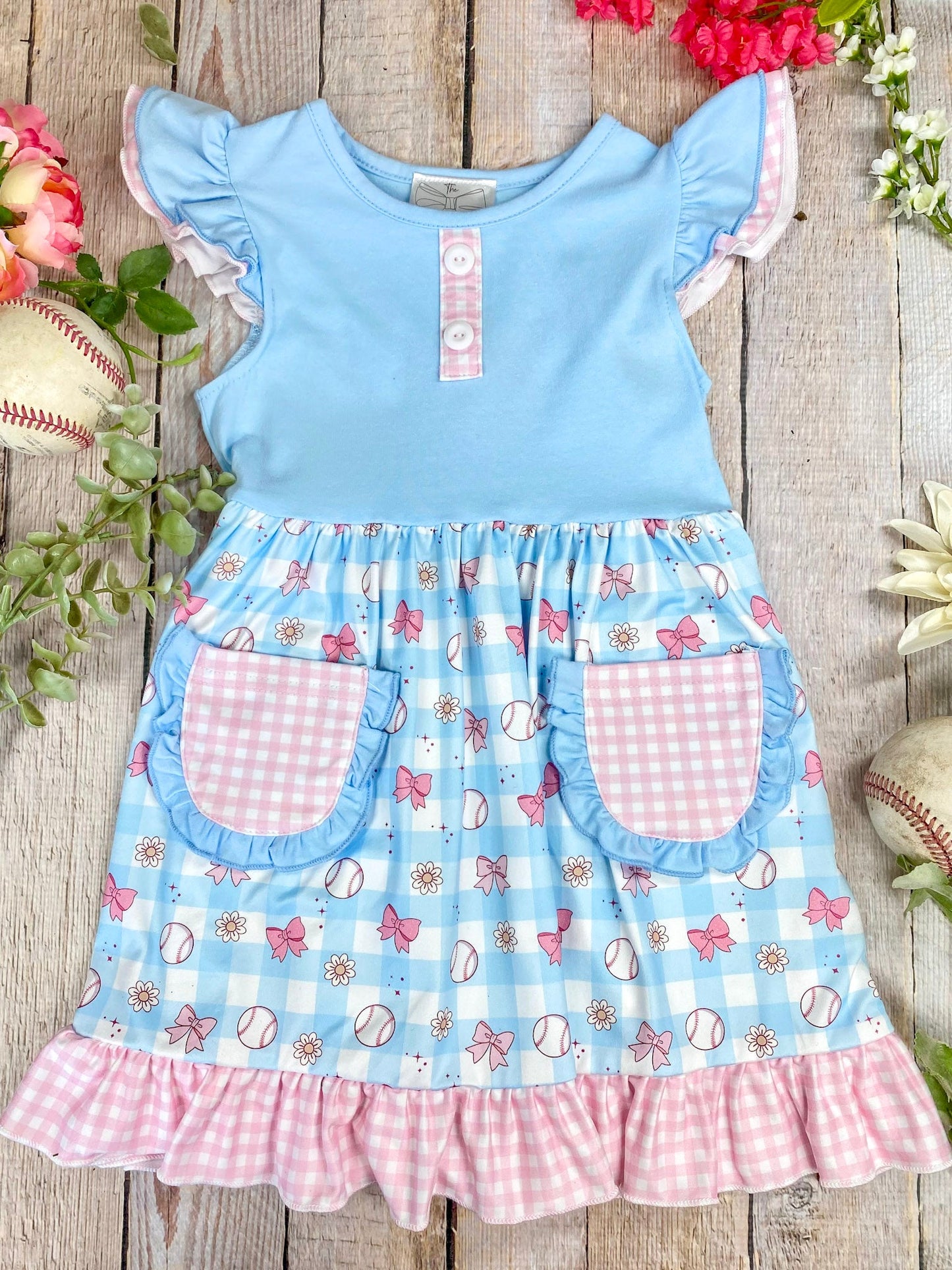 Children's dress with blue top and checkered skirt on a wooden surface with flowers and baseballs.