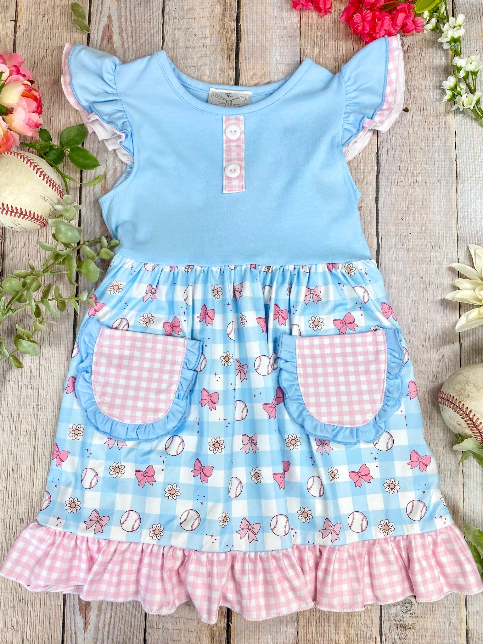 Children's dress with blue top and checkered skirt on a wooden surface with flowers and baseballs.