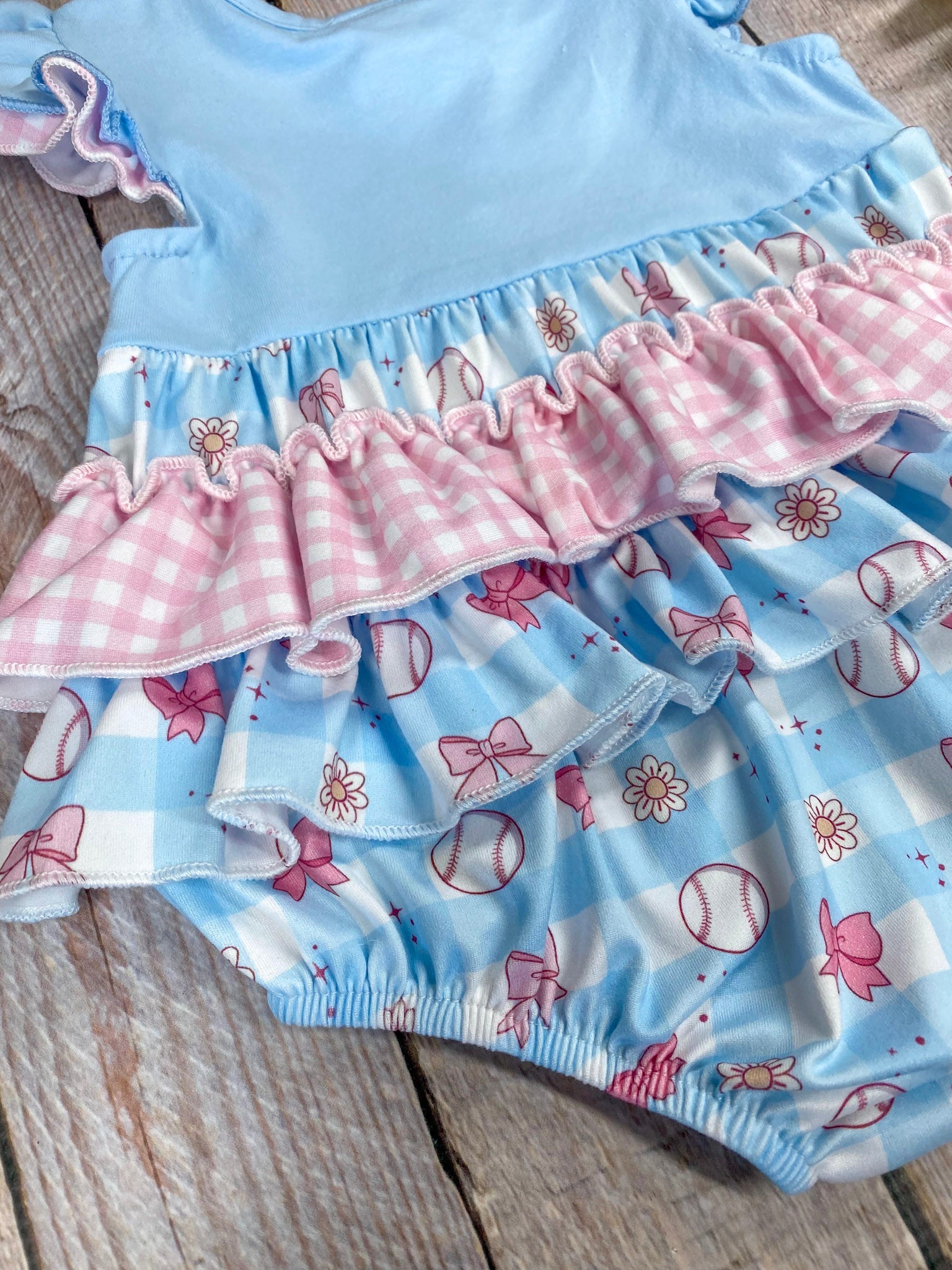 Baby romper with blue top and pink ruffles on a wooden background