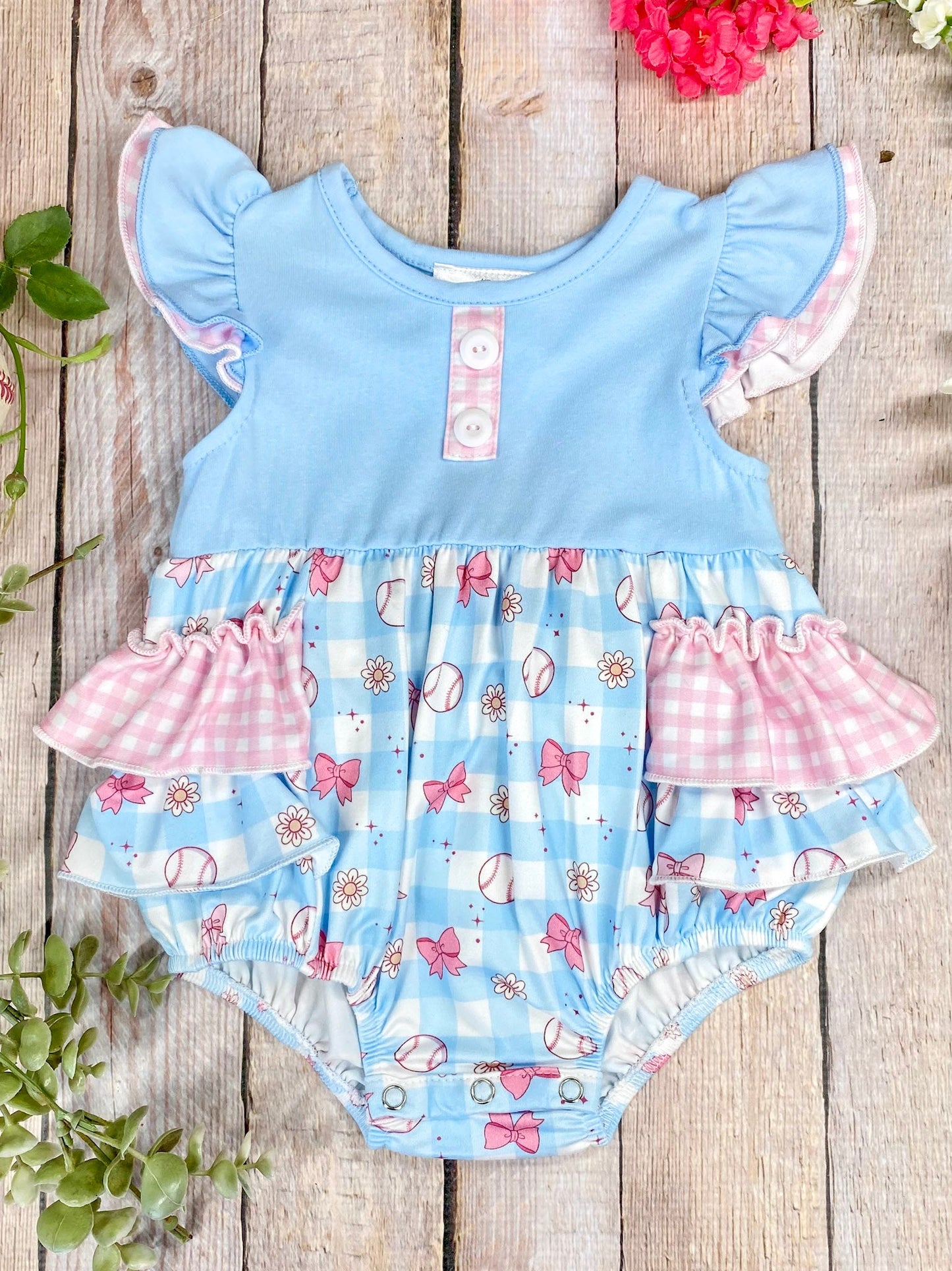 Baby romper with blue top and pink ruffles on a wooden background