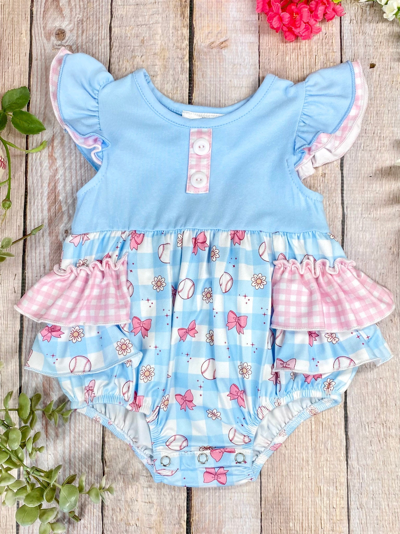 Baby romper with blue top and pink ruffles on a wooden background