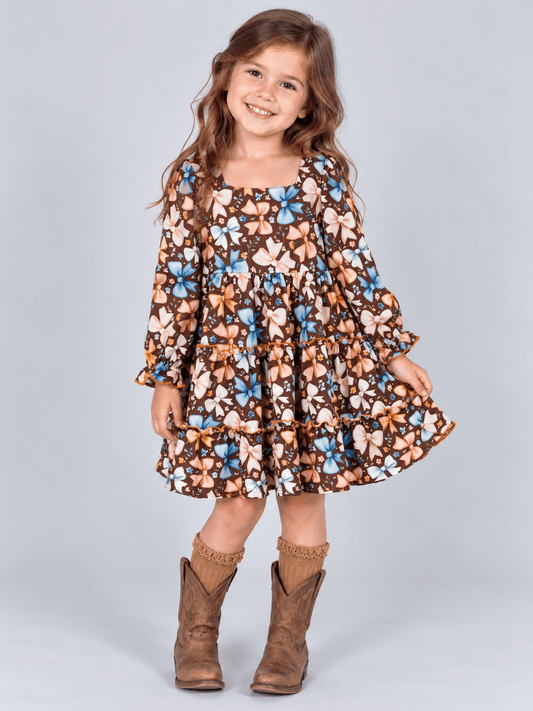 model wearing Girls brown bow print tiered dress with long sleeves and ruffle details