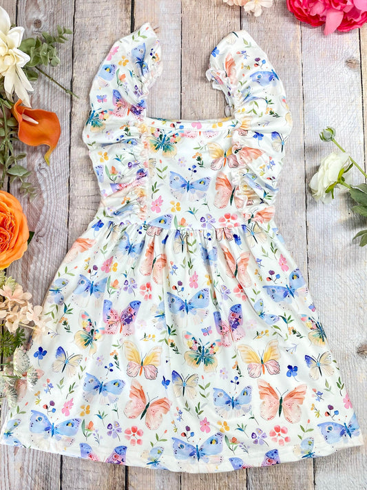 Floral dress with butterfly pattern on a wooden surface with flowers around