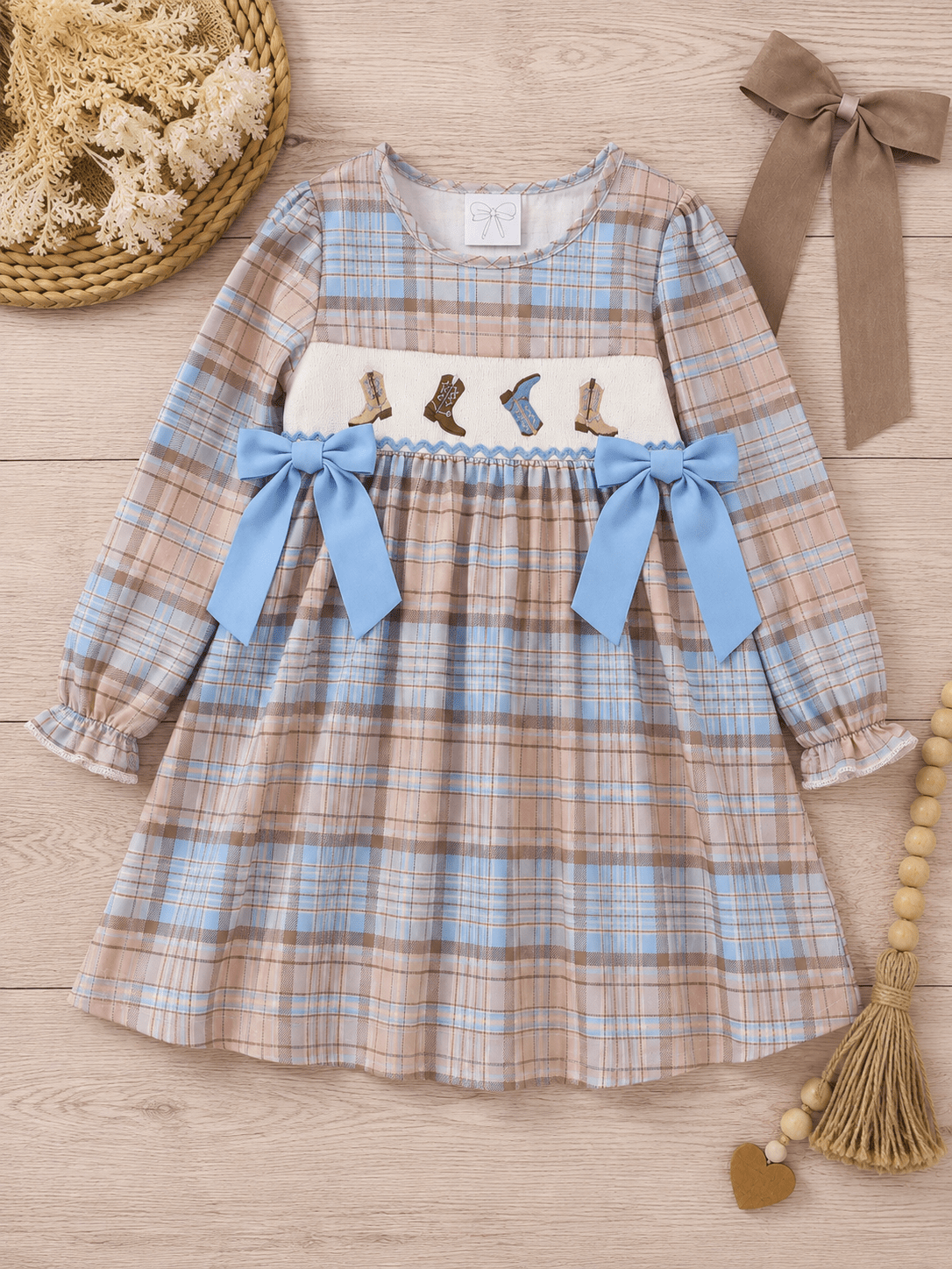Girls pastel plaid smocked cowboy boots dress with blue bows and embroidered western boots on a neutral wood flat lay, boutique long sleeve toddler and girls fall dress.