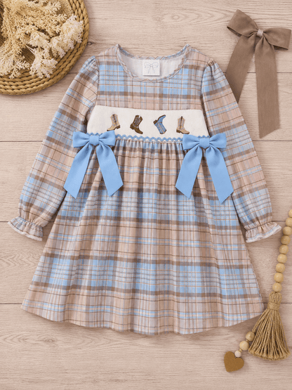 Girls pastel plaid smocked cowboy boots dress with blue bows and embroidered western boots on a neutral wood flat lay, boutique long sleeve toddler and girls fall dress.