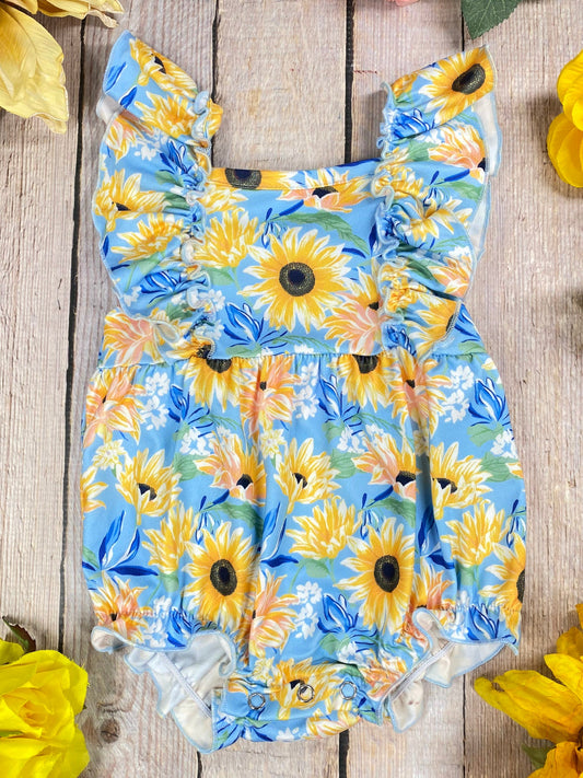 Sunflower-patterned romper on a wooden surface with sunflowers around