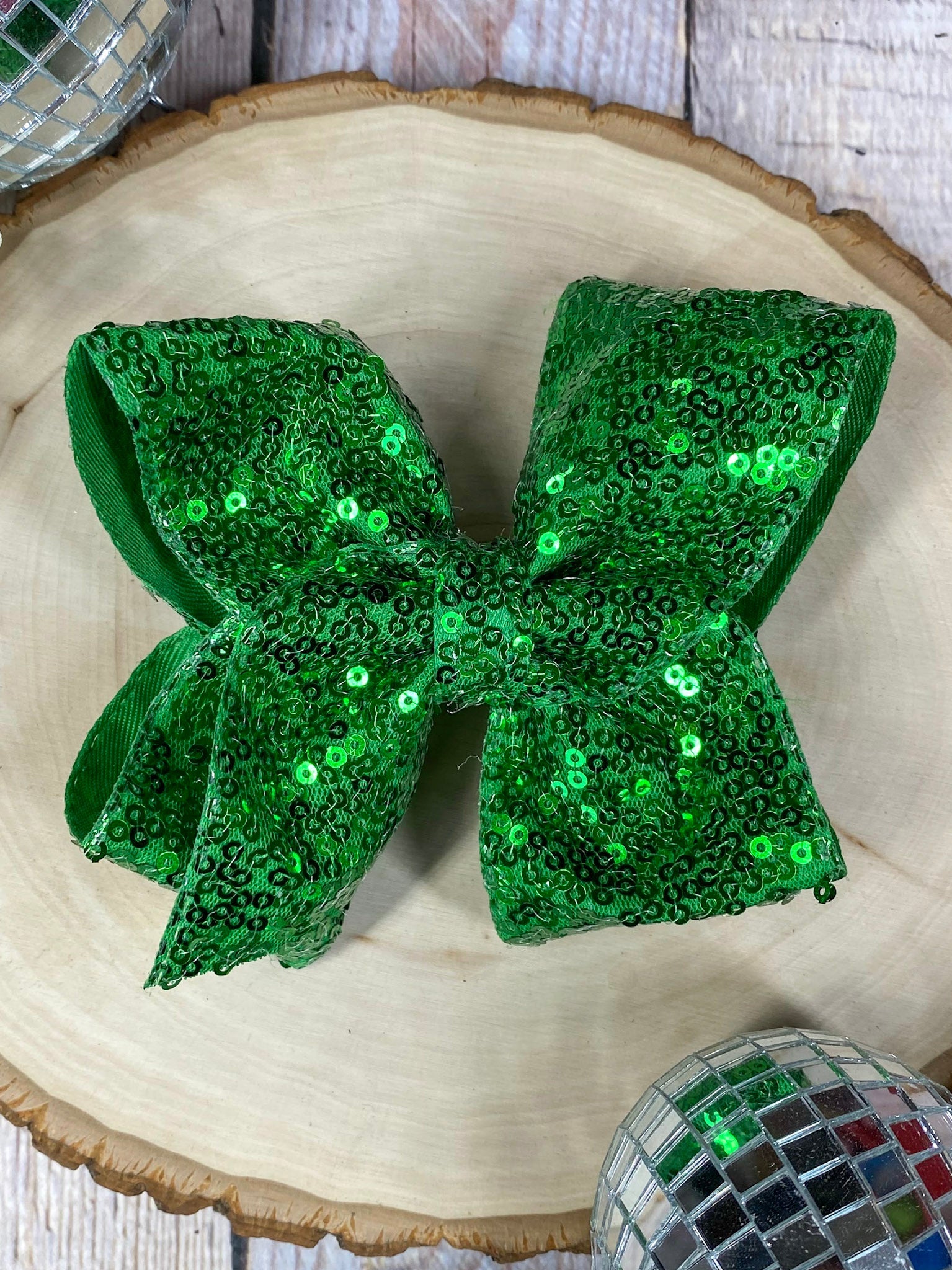Green sequin bow on a wooden surface with a disco ball in the background