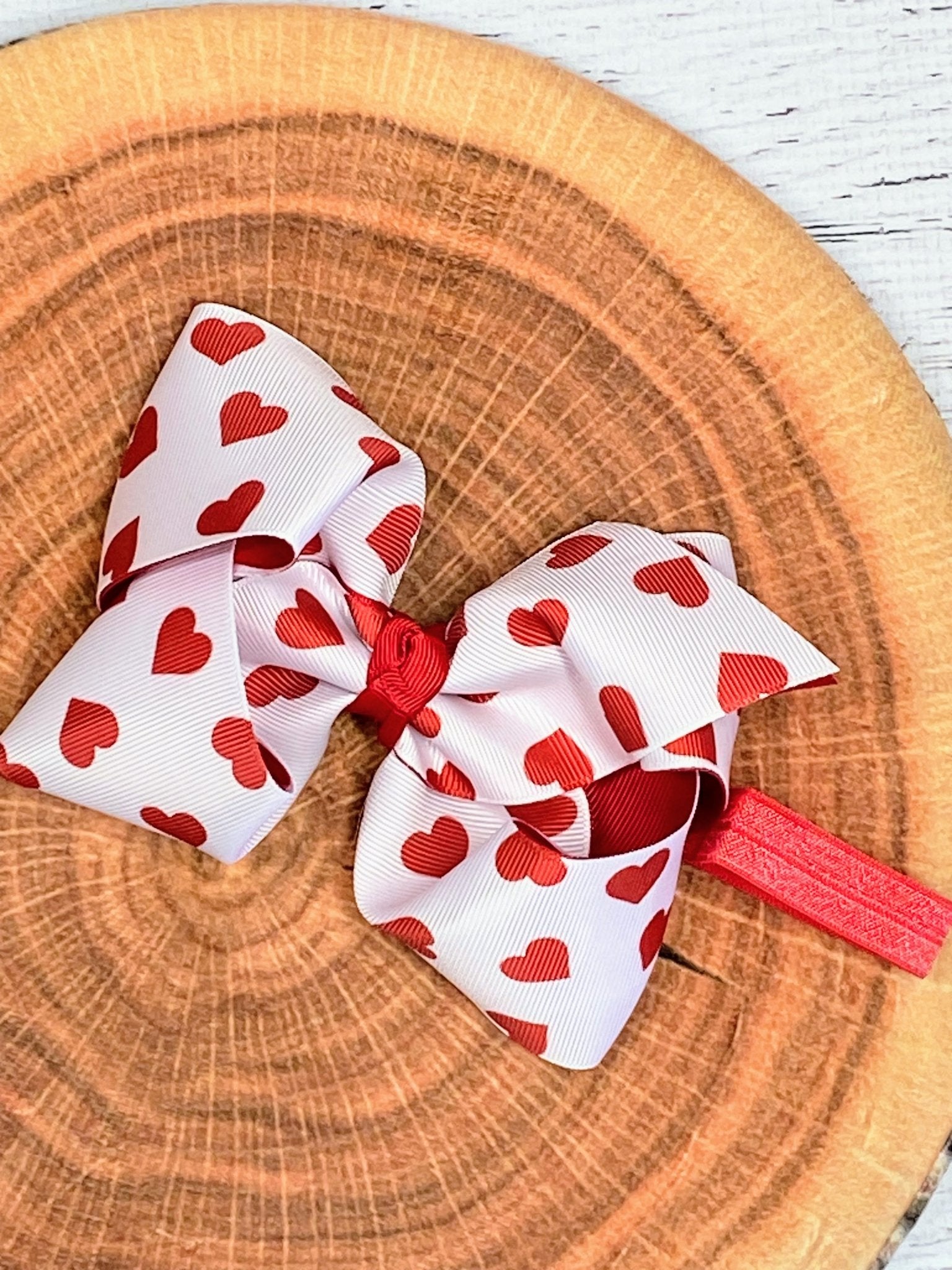 Valentine heart print white hair bow headband with red bow on wooden background – cute girls accessory from The Hair Bow Company