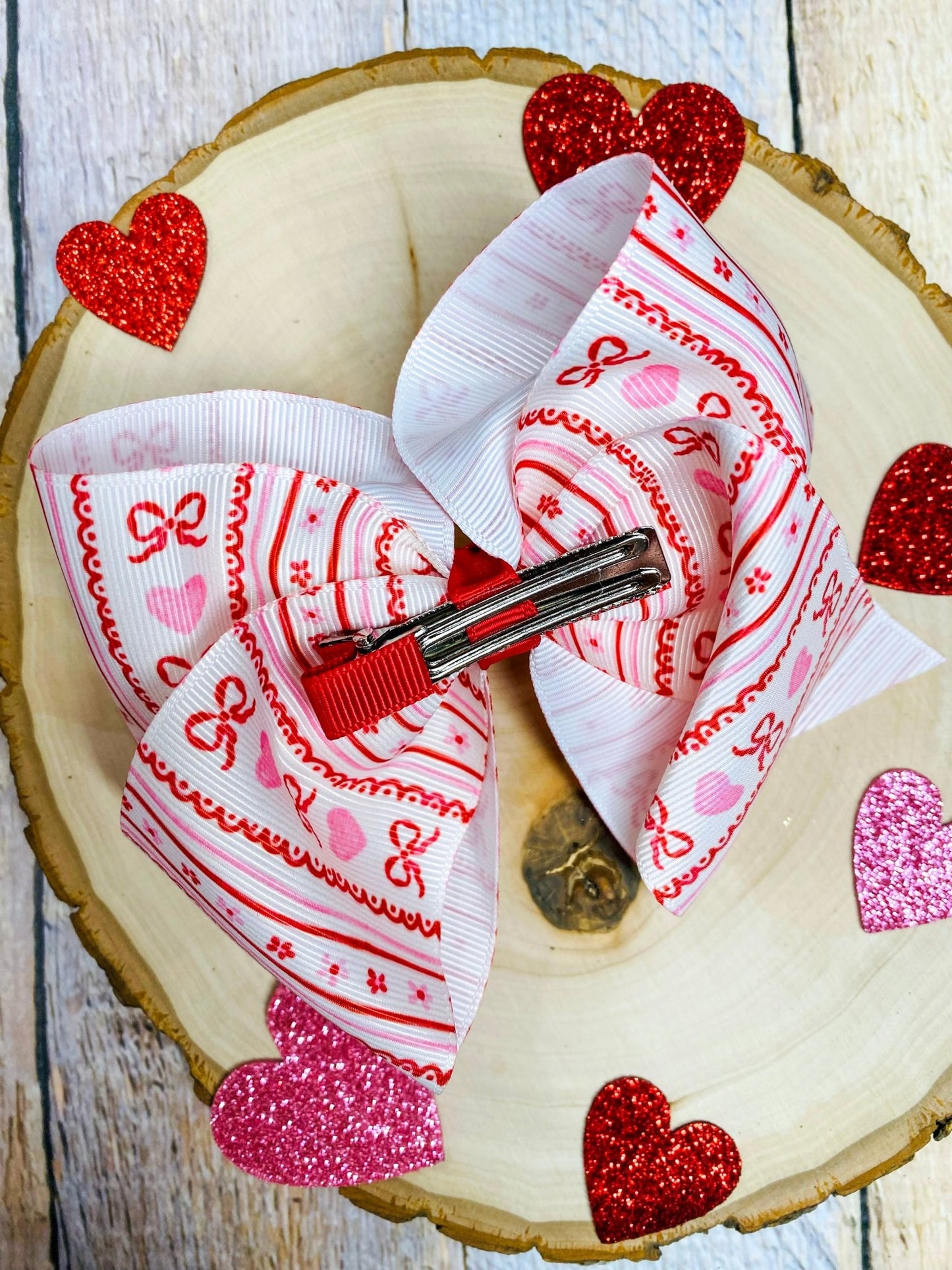 Decorative hair bow with red and white pattern on a wooden surface with heart-shaped decorations.