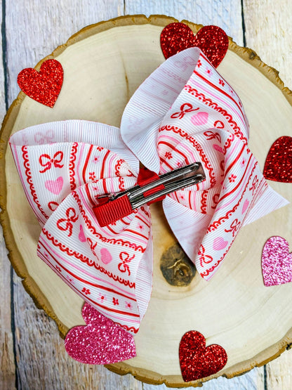 Decorative hair bow with red and white pattern on a wooden surface with heart-shaped decorations.