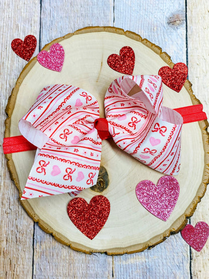 Two hair bows with red and pink patterns on a wooden slice with heart decorations.