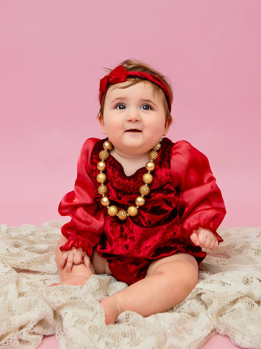 Baby wearing a red velvet holiday onesie and bow headband