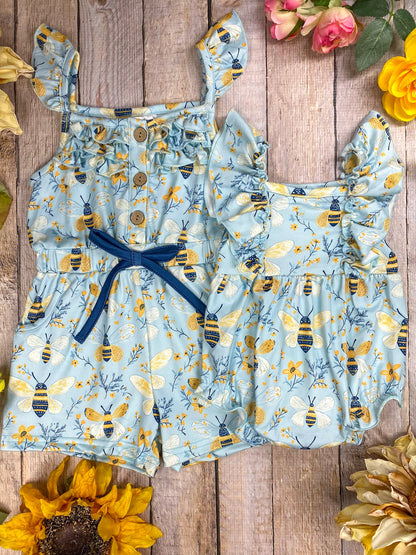 Children's romper sibling set with bee pattern on a wooden surface with flowers.