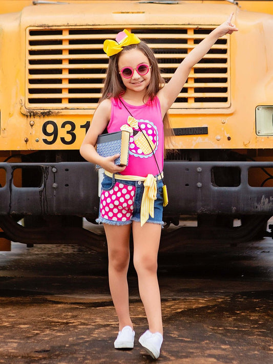 A child standing in front of a yellow school bus, wearing a hot pink pencil tank top with a character design and denim shorts.