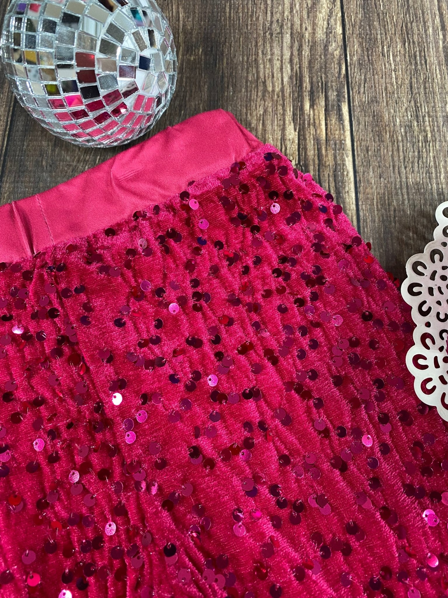 Close-up of a red sequined fabric with a disco ball and doily on a wooden surface