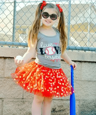Child wearing a red and gray outfit with a tutu, standing outdoors.