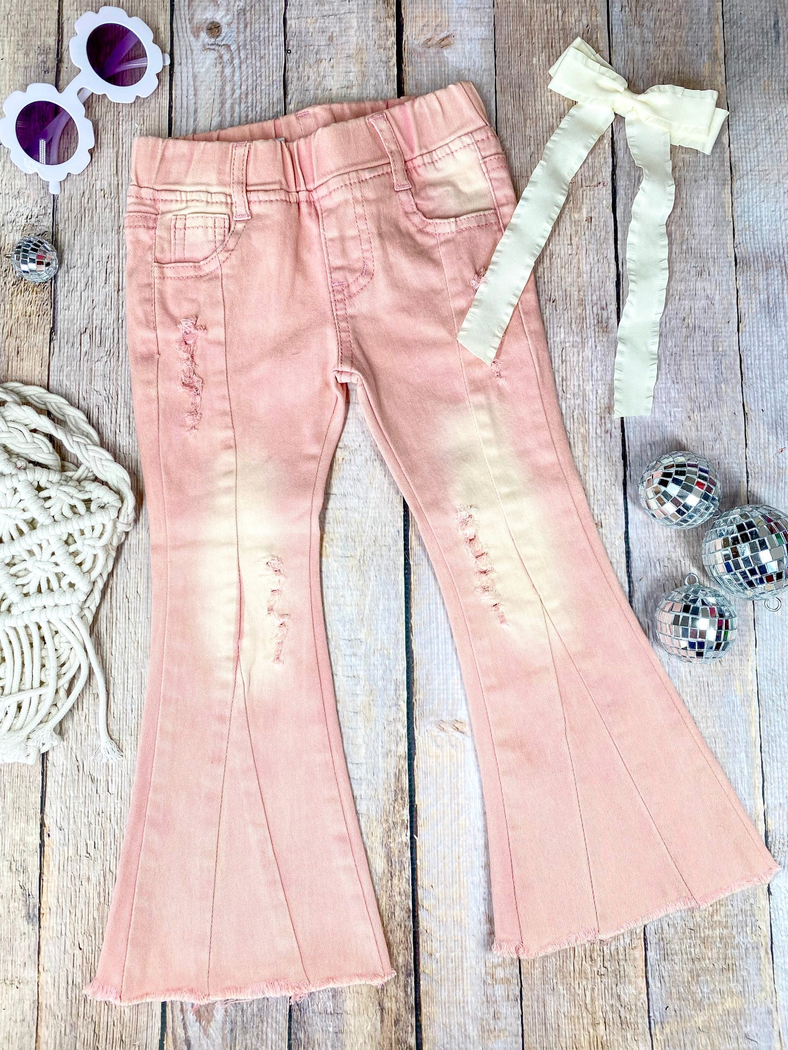 Pink flared jeans with slight distressing on a wooden background