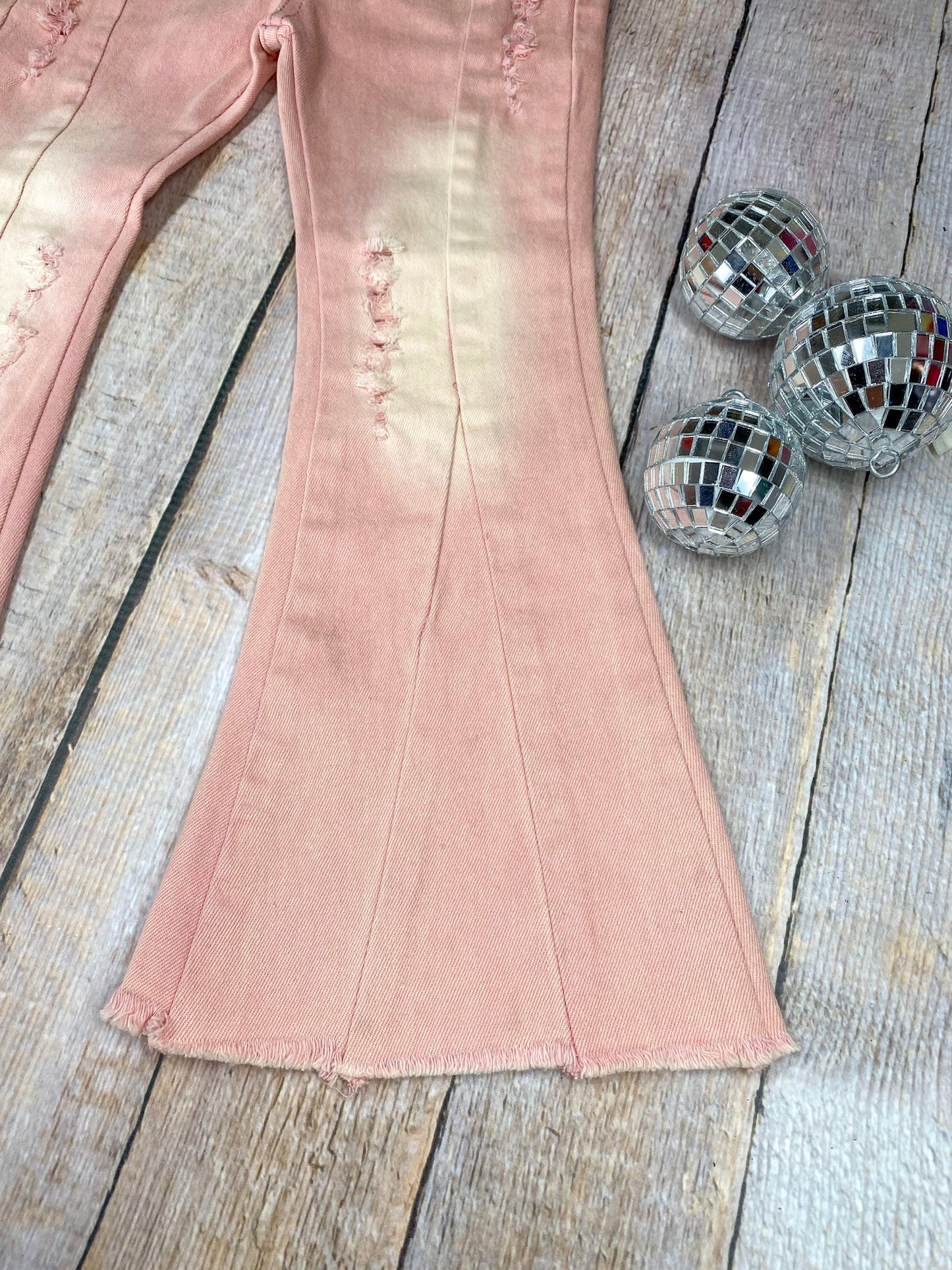 Pink flared jeans with slight distressing on a wooden background