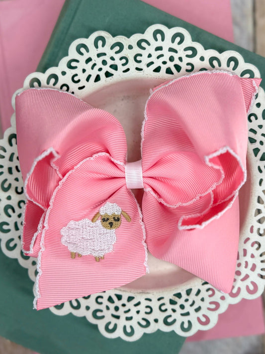 Light pink grosgrain hair bow with moonstitch edging and embroidered lamb detail on a decorative background