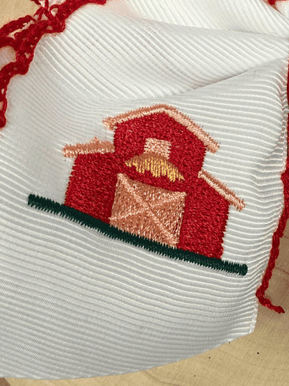 Close-up of red farmhouse barn embroidery on white grosgrain hair bow