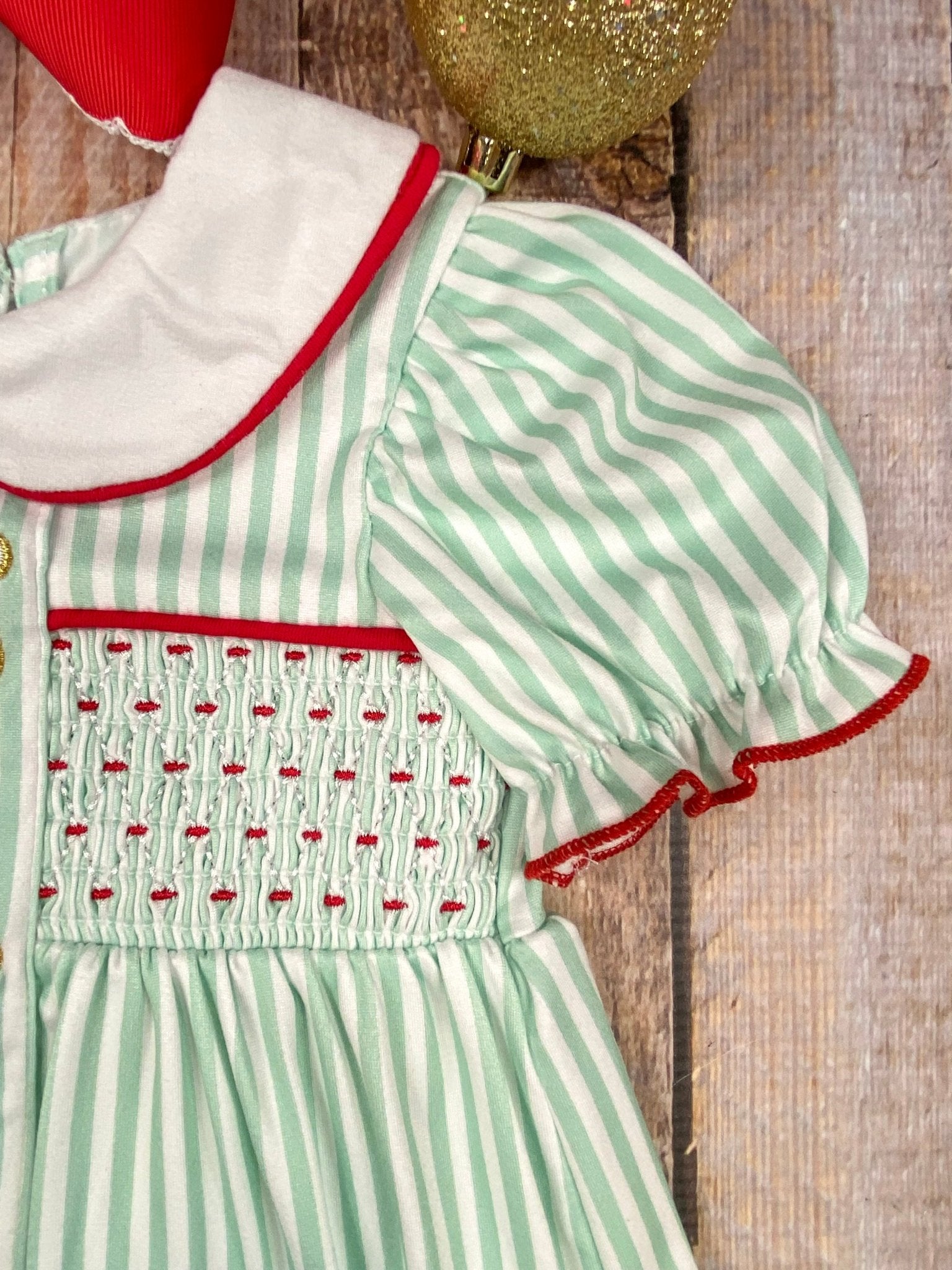 Green and white striped Christmas dress with red trim on a wooden surface