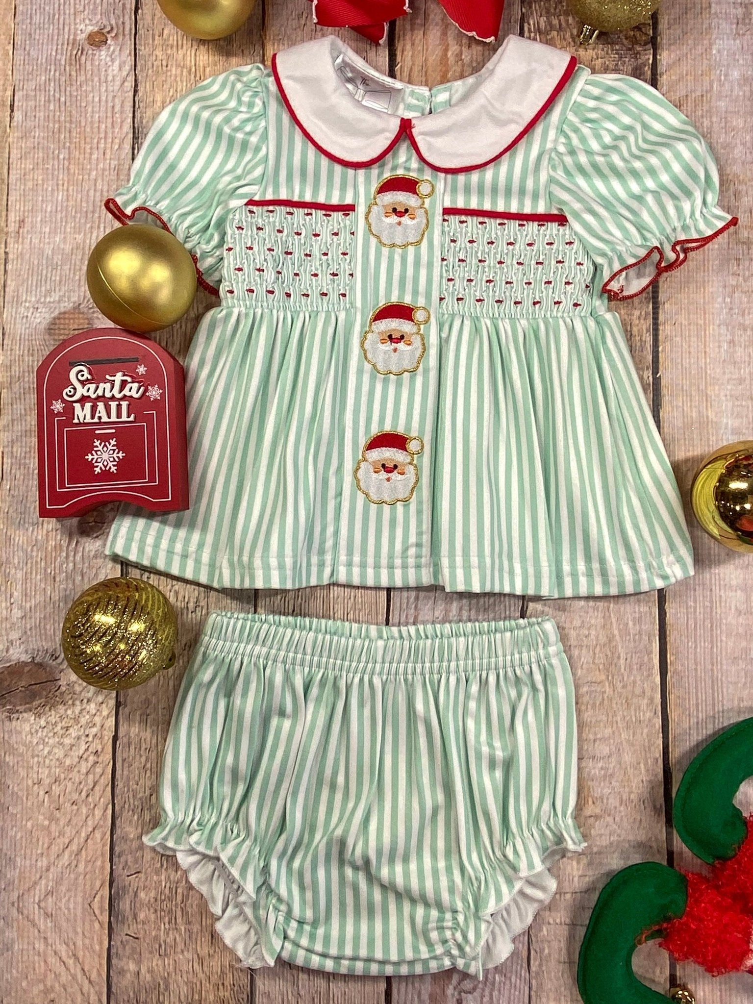 Children's Christmas outfit with green and white striped top and bloomers on a wooden surface.