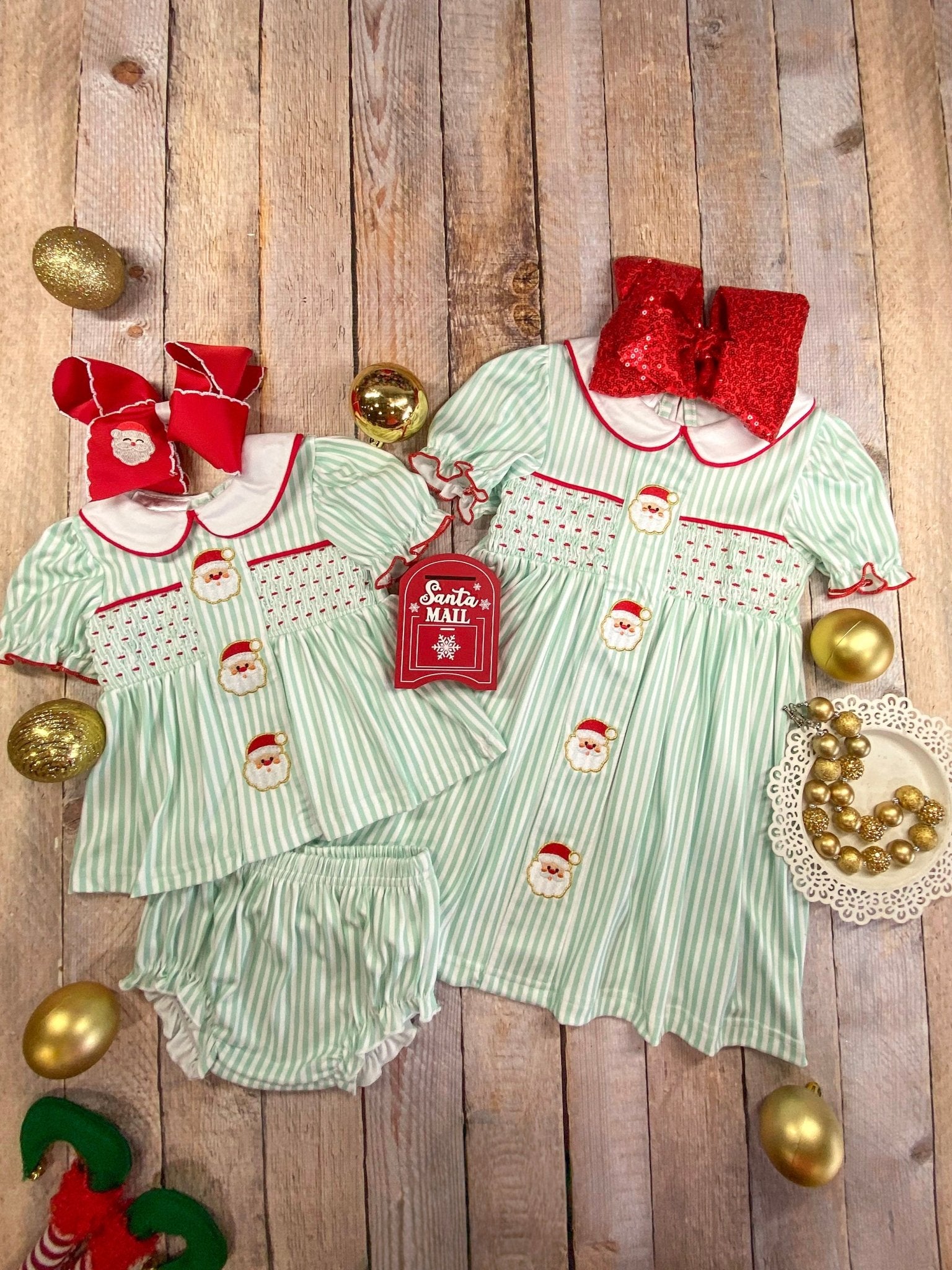 Children's Christmas outfit with green and white striped dress, red bows, and gold ornaments on a wooden background.