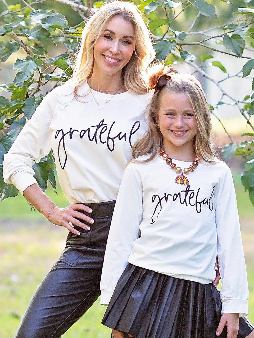 Mom and daughter in matching Grateful shirts under a tree