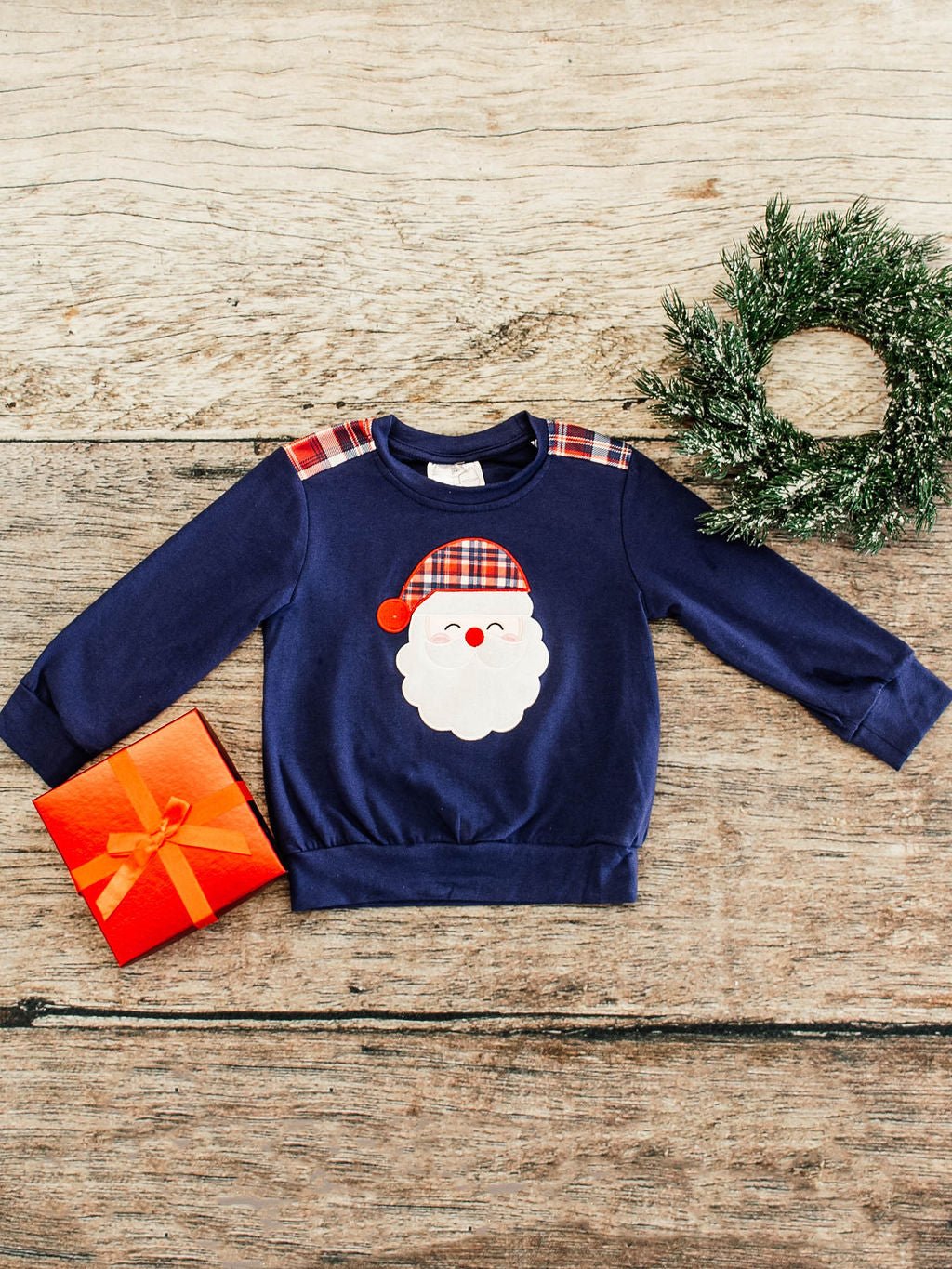 navy long sleeve flay lay with a santa wearing a red, navy, and white plaid hat applique on center of shirt with same plaid details also on shoulders