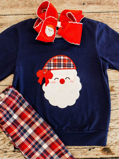 close up of a navy long sleeve with a santa wearing a plaid hat applique on the center and red, navy, plaid pants showing in corner, styled with red bow featuring a santa embroidery on it