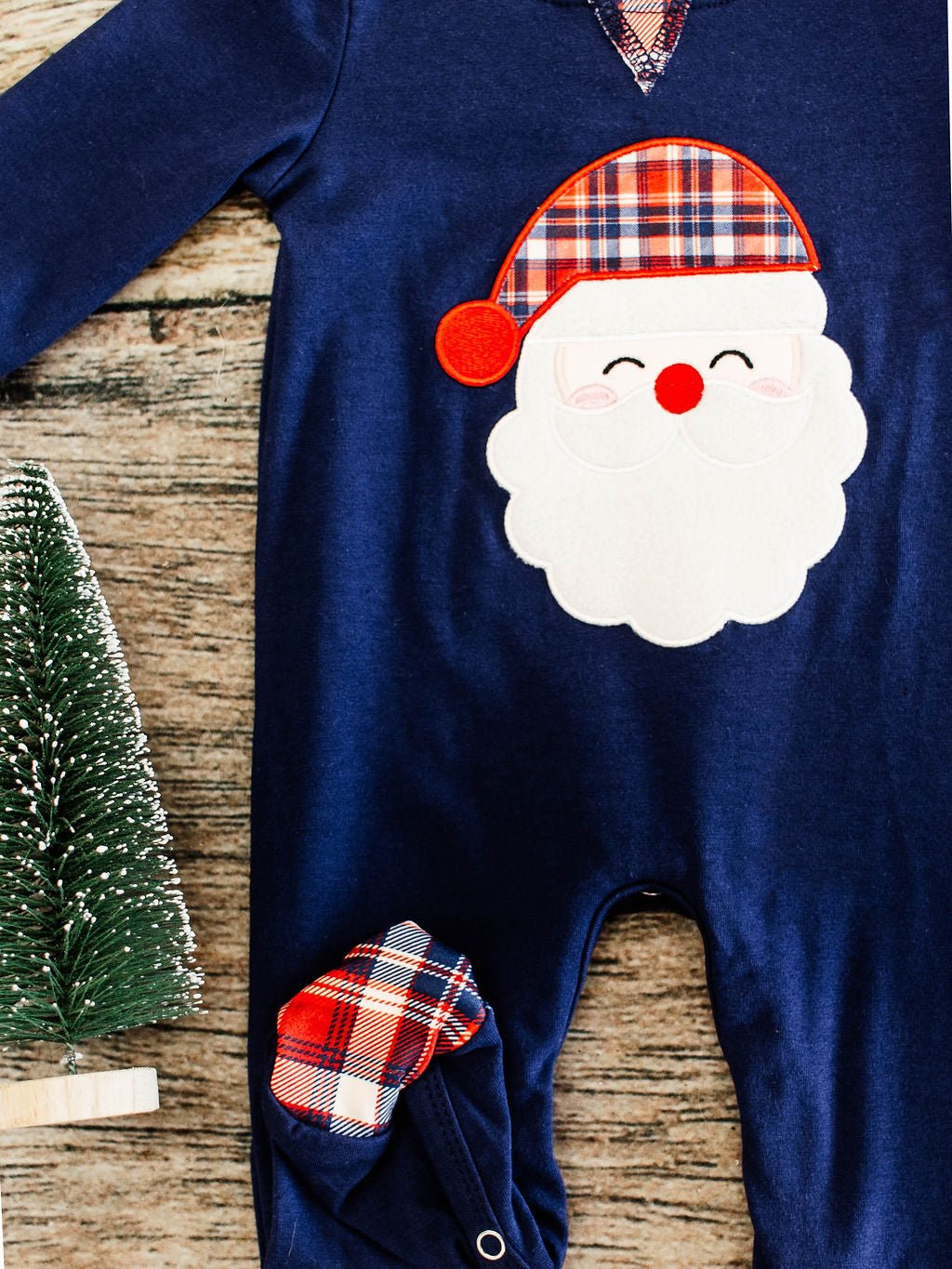 close up showing the navy romper with santa wearing plaid hat applique and plaid footie folded upwards